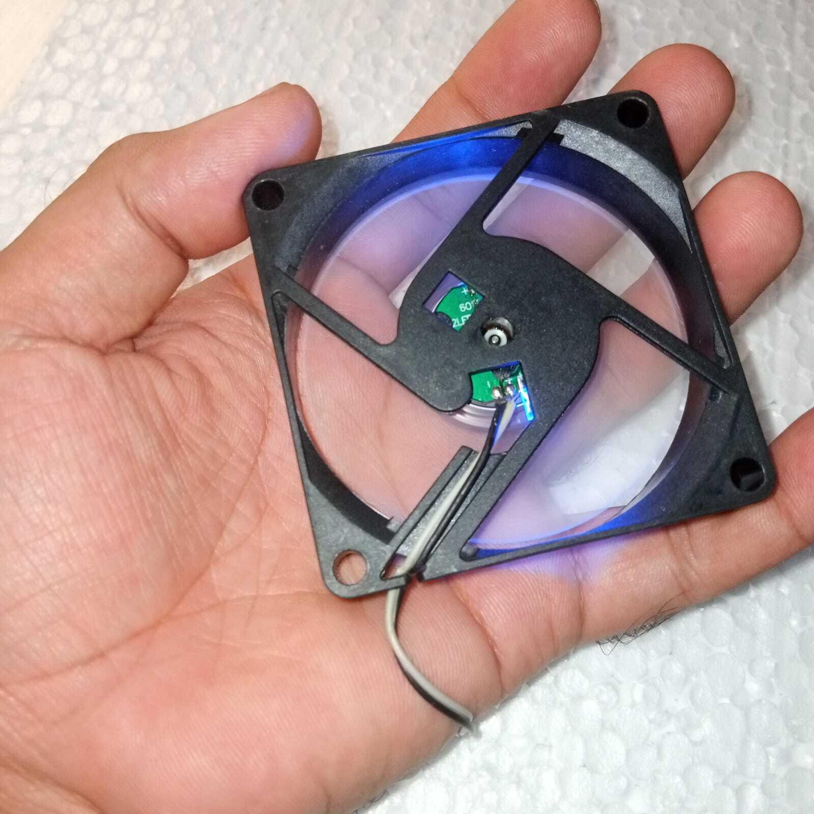 5V Fan With LED - held in a hand, showing a square black frame with a clear fan blade, internal green circuit board, and a two-wire power cable.