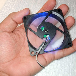 5V Fan With LED - held in a hand, showing a square black frame with a clear fan blade, internal green circuit board, and a two-wire power cable.