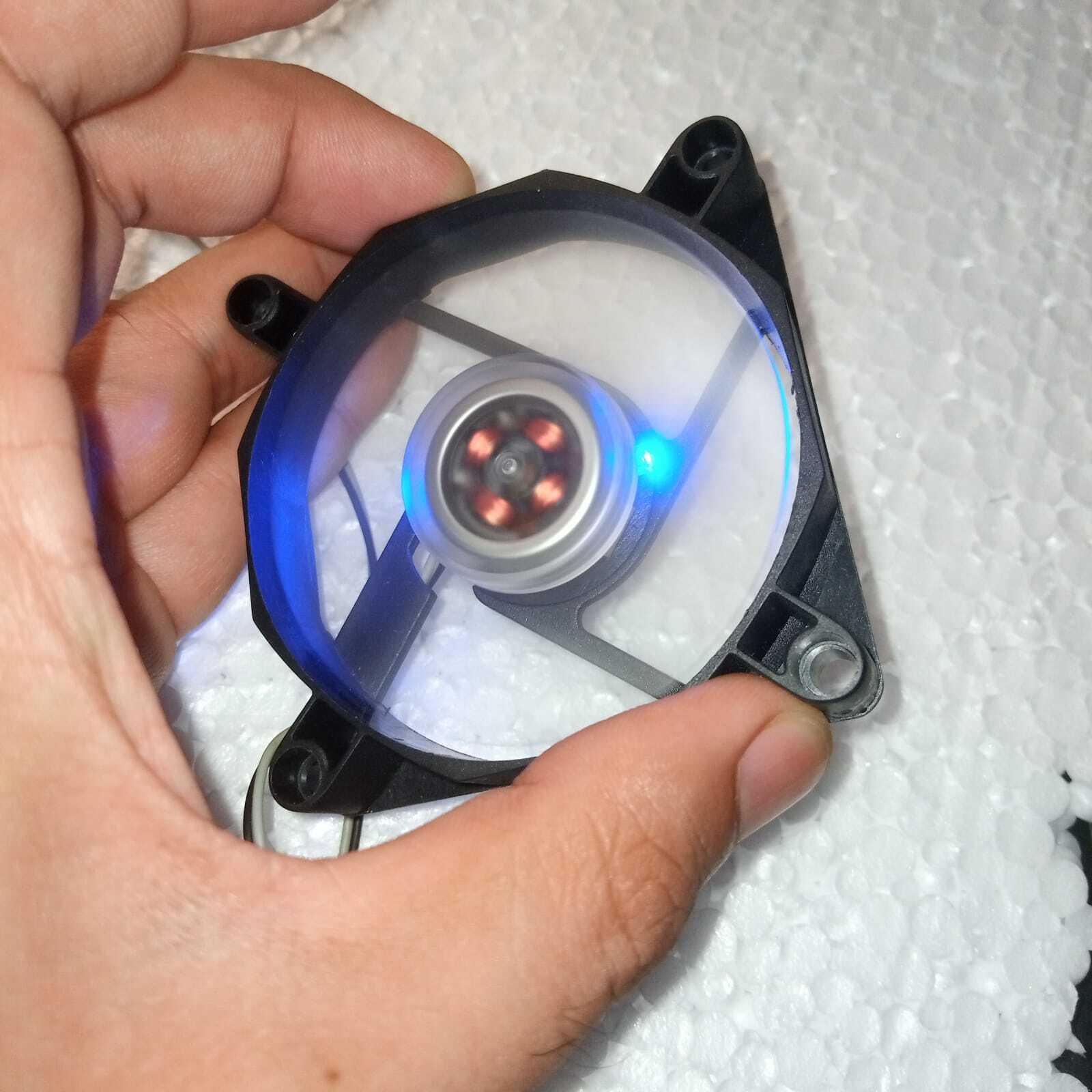 5V Fan With LED - shown being held in a hand, featuring a circular black frame, a transparent blade assembly, and an active blue LED indicator light.