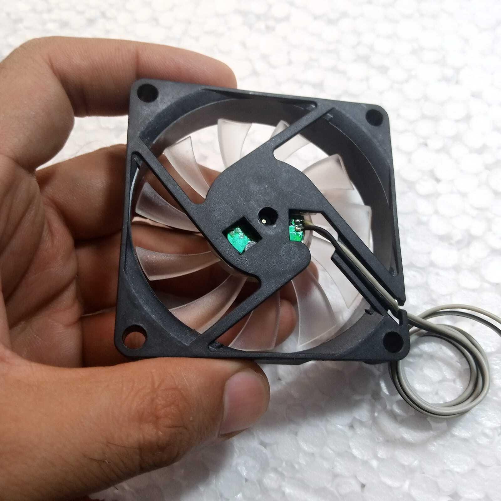 5V Fan With LED - shown from the back, featuring a black square frame, clear fan blades, and a two-wire connector cable held in a hand.