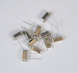 6.144M 6.144MHz Crystal Oscillator For Solar Inverter - a pile of silver, rectangular, two-pin metal components on a white background.