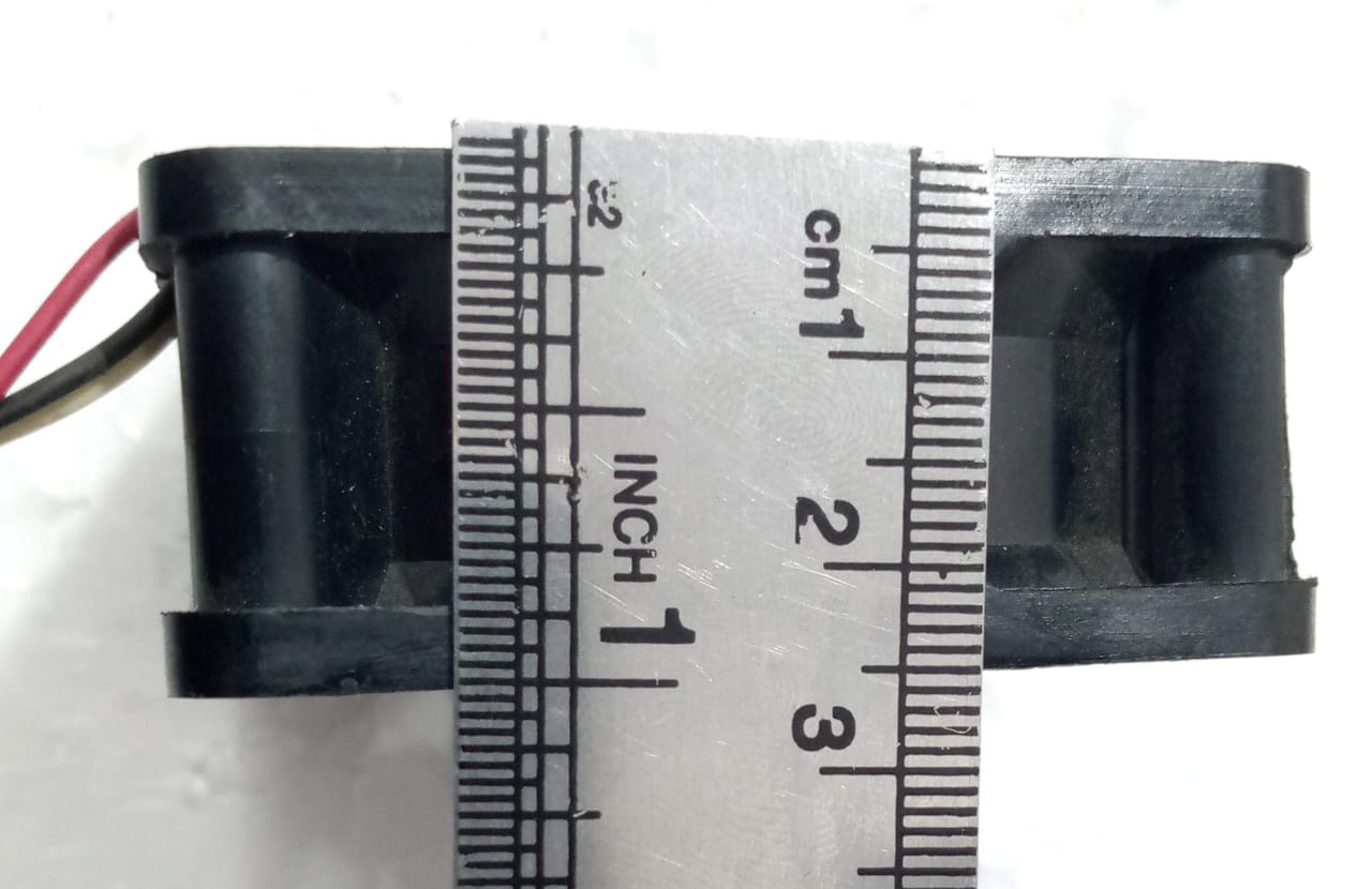 60mm x 60mm 24V Cooling Fan For Computer And Other Electronic Devices - Digilog.pk - a close-up view showing the black square fan housing being measured by a metal ruler in centimeters and inches.