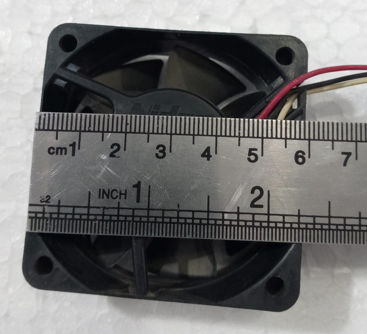 60mm x 60mm 24V Cooling Fan For Computer And Other Electronic Devices - Digilog.pk - shown from a top-down view with a metal ruler measuring its width in centimeters.
