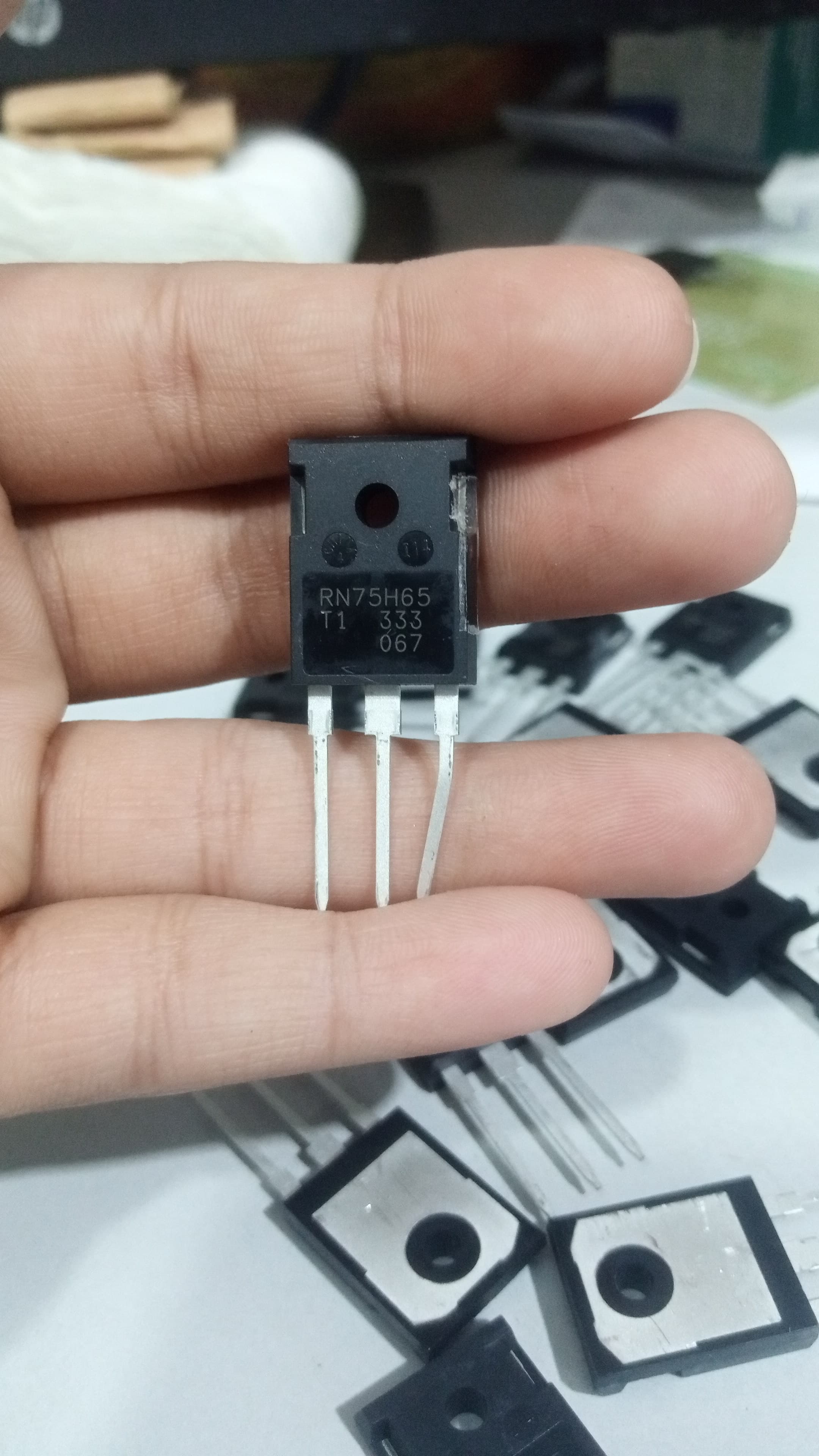 650V 75A RN75H65 RBN75H65T1 IGBT Insulated-gate Bipolar Transistor - a black three-pin electronic component held in a hand with multiple identical units scattered on a white surface in the background.