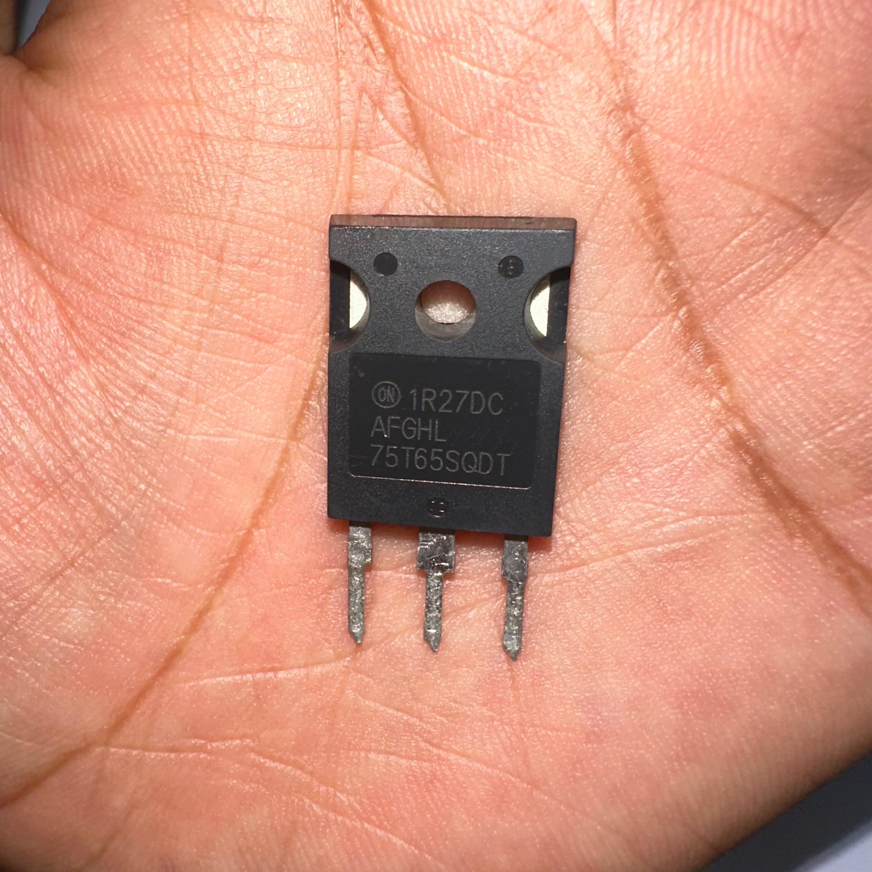 75A 650V On Semiconductor 75T65SQDT IGBT With Soft Fast Recovery Diode-digilog.pk - close-up view of a black, three-pin semiconductor component held in a palm, showing the text 1R27DC, AFGHL, and 75T65SQDT printed on it.