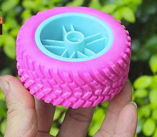 75mm Robot Climbing Car Tire Tyre Wheel Hollow Good Elasticity DIY Toy Chassis Accesso - a close-up of a pink rubber tire with a blue plastic wheel hub held in a hand against a blurred green background.