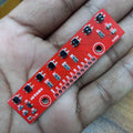8 Channel Reflectance Sensor Array Module Qtr-8A - a red rectangular circuit board with eight sensors and a row of labeled pin headers held in a hand.