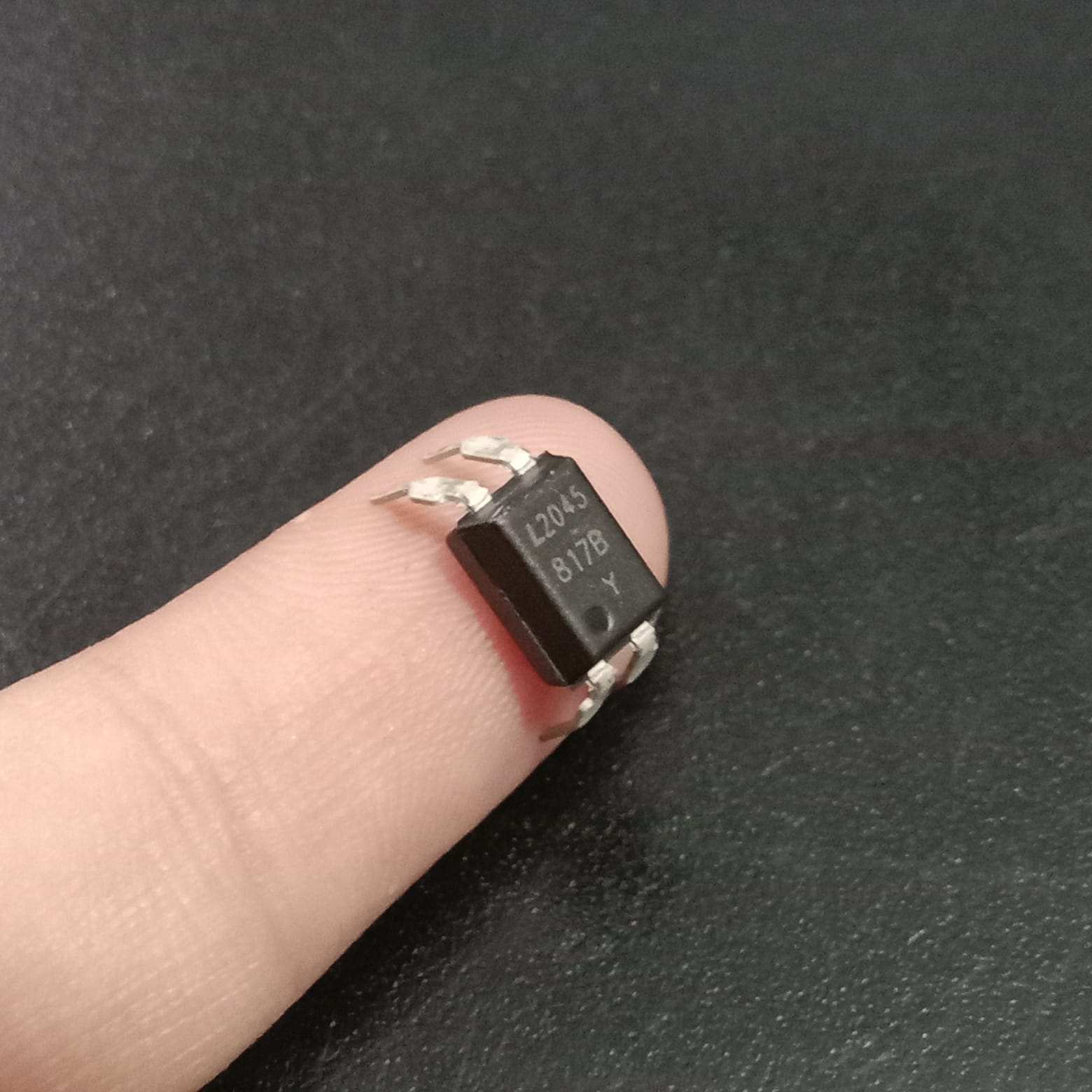 817B Optocoupler - a black, four-pin electronic component held on a finger, featuring the markings L2045, 817B, and Y on its top surface.