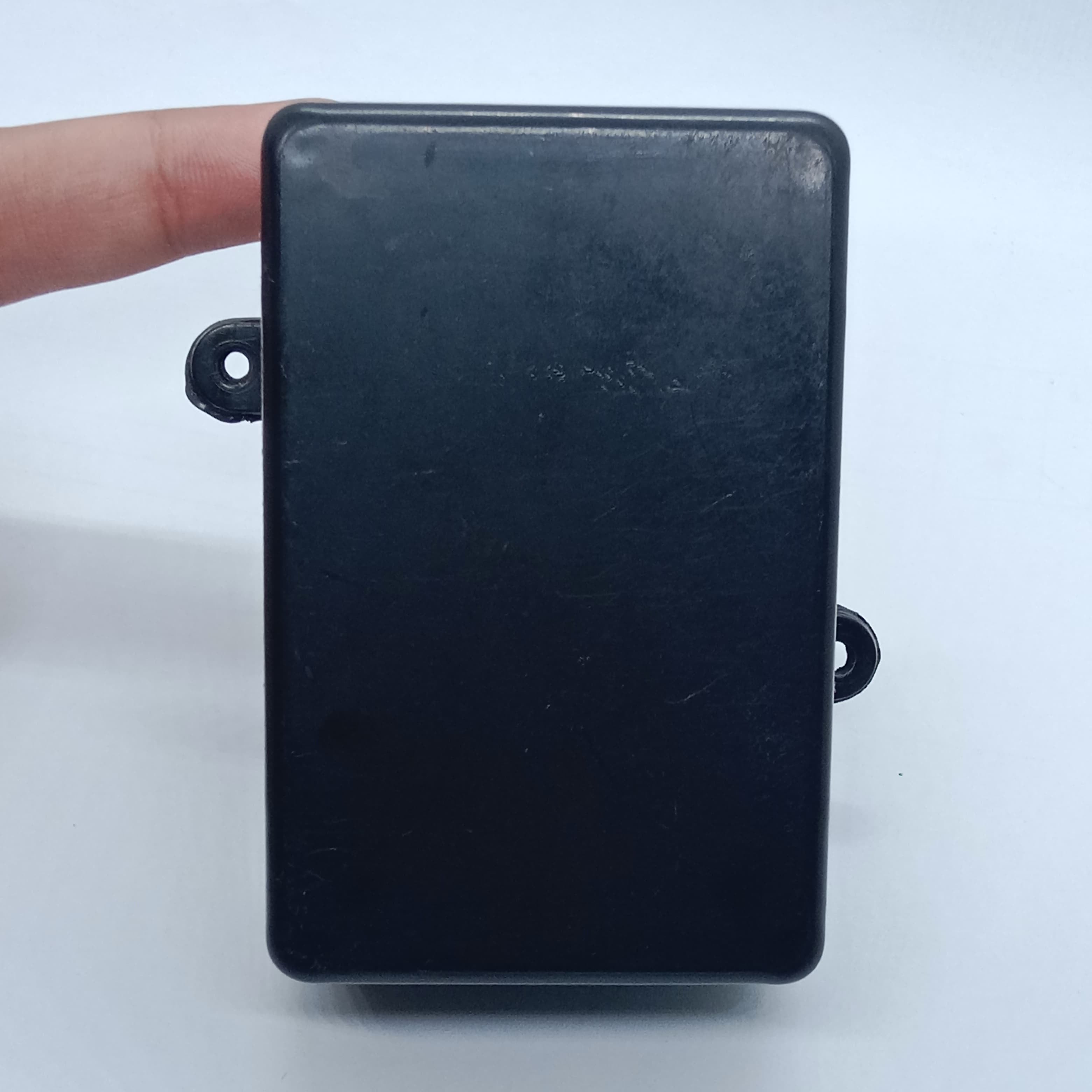 87mm x 55mm X33MM ABS Box PCB Enclosure Plastic Box Project Box - a plain black rectangular plastic project box with two mounting tabs on the sides, held by a finger.