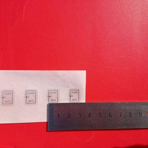 915MHz Uhf Mini RFID Tag - shown as four small rectangular white stickers labeled "ALIEN 9613" next to a metal ruler on a red surface for scale.