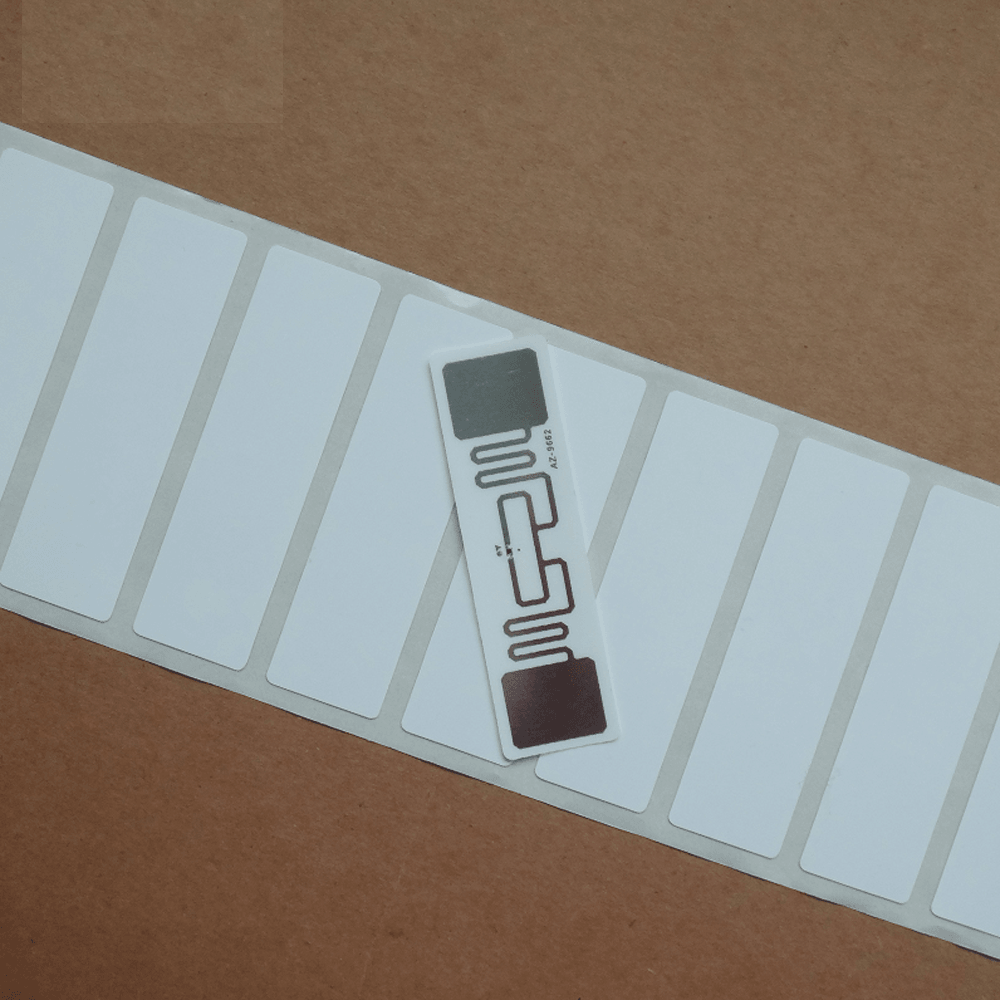 915MHz Uhf Passive RFID Tag Uhf RFID Tag Alien Higgs 3 9662 Epc Global C1G2 Dry Inlay Printable - a single white rectangular adhesive label with a visible copper antenna pattern resting on a roll of similar labels.