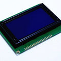 JHD12864E Blue Color 128 By 64 Graphical LCD - a rectangular module with a blue screen mounted on a green circuit board featuring a row of pins.