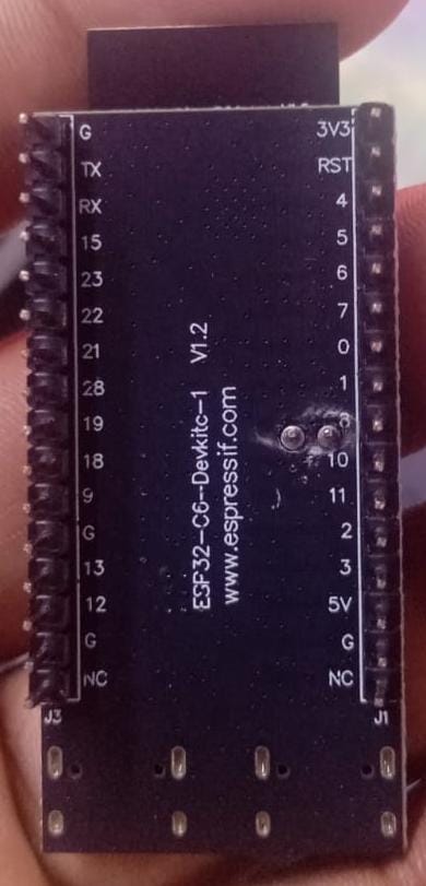 A close-up of a black electronic module labeled ESP32-C6-DevKit-V1 v1.2 with pin markings and a website URL, held in a person's hand.