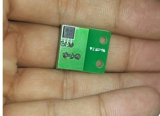 A1104E A04E New Original Hall Monopole Switch Small Volume TO-92uA - shown as a close-up of a small green circuit board with a black electronic component held in a person's hand.