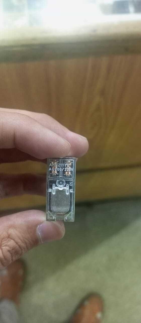AC Relay Coil AC220V AHN211YO - a close-up view of a small, transparent rectangular relay held by fingers, showing the printed model and voltage label.