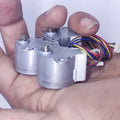 Arduino 5V Stepper Motor 24BYJ - two silver cylindrical stepper motors held in a hand, each with a white connector and multi-colored wires.
