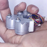 Arduino 5V Stepper Motor 24BYJ - two silver cylindrical stepper motors held in a hand, each with a white connector and multi-colored wires.