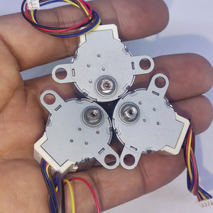 Arduino 5V Stepper Motor 24BYJ - shown as three silver circular motors with white plastic connectors and multi-coloured wires held in a hand.
