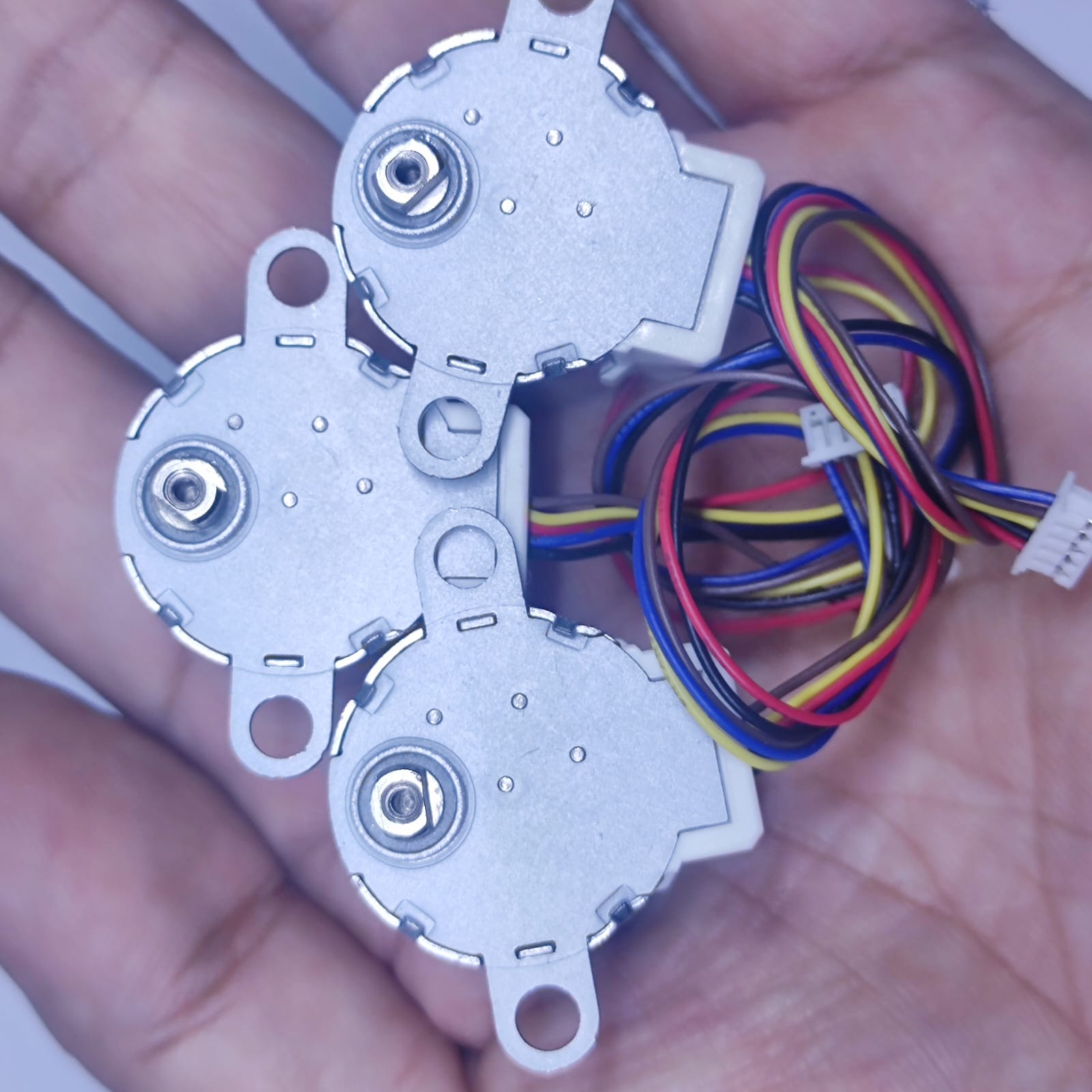 Arduino 5V Stepper Motor 24BYJ - three silver circular motors held in a hand, each with a white connector and multi-coloured wiring harness.