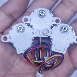 Arduino 5V Stepper Motor 24BYJ - three silver circular motors held in a hand, each with a white connector and multi-coloured wiring harness.