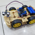 Arduino Obstacle Avoiding Robot Parts - an assembled four-wheeled yellow and black chassis with an ultrasonic sensor, motor driver board, and battery pack.