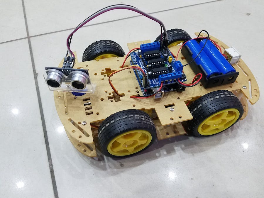 Arduino Obstacle Avoiding Robot Parts - an assembled four-wheeled yellow and black chassis with an ultrasonic sensor, motor driver board, and battery pack.