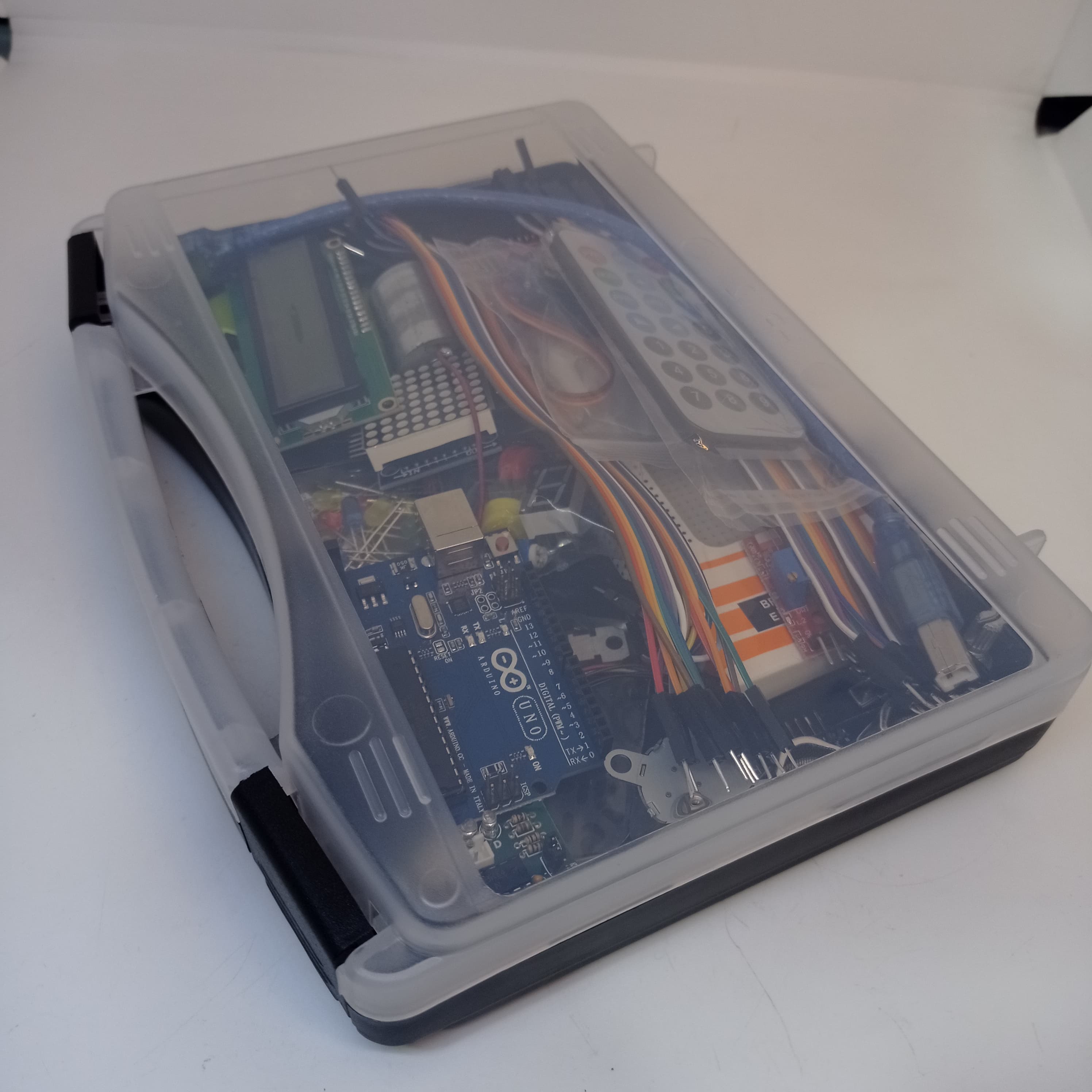 Arduino Starter Kit - clear plastic carrying case containing an Arduino Uno board, an LCD module, jumper wires, and various electronic components.