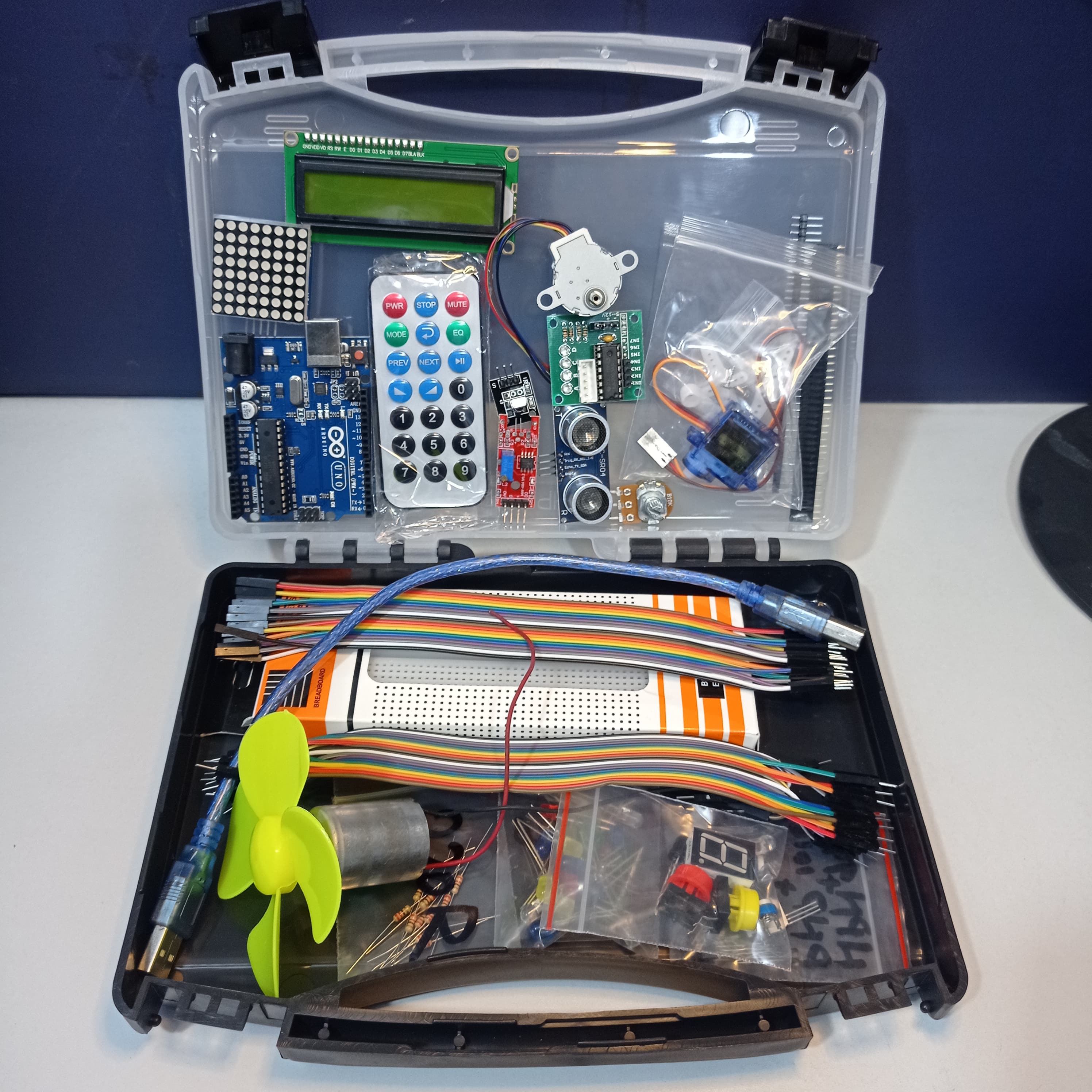 Arduino Starter Kit - shown in a clear plastic carrying case containing an Arduino Uno board, LCD screen, remote control, breadboard, cables, and motor.