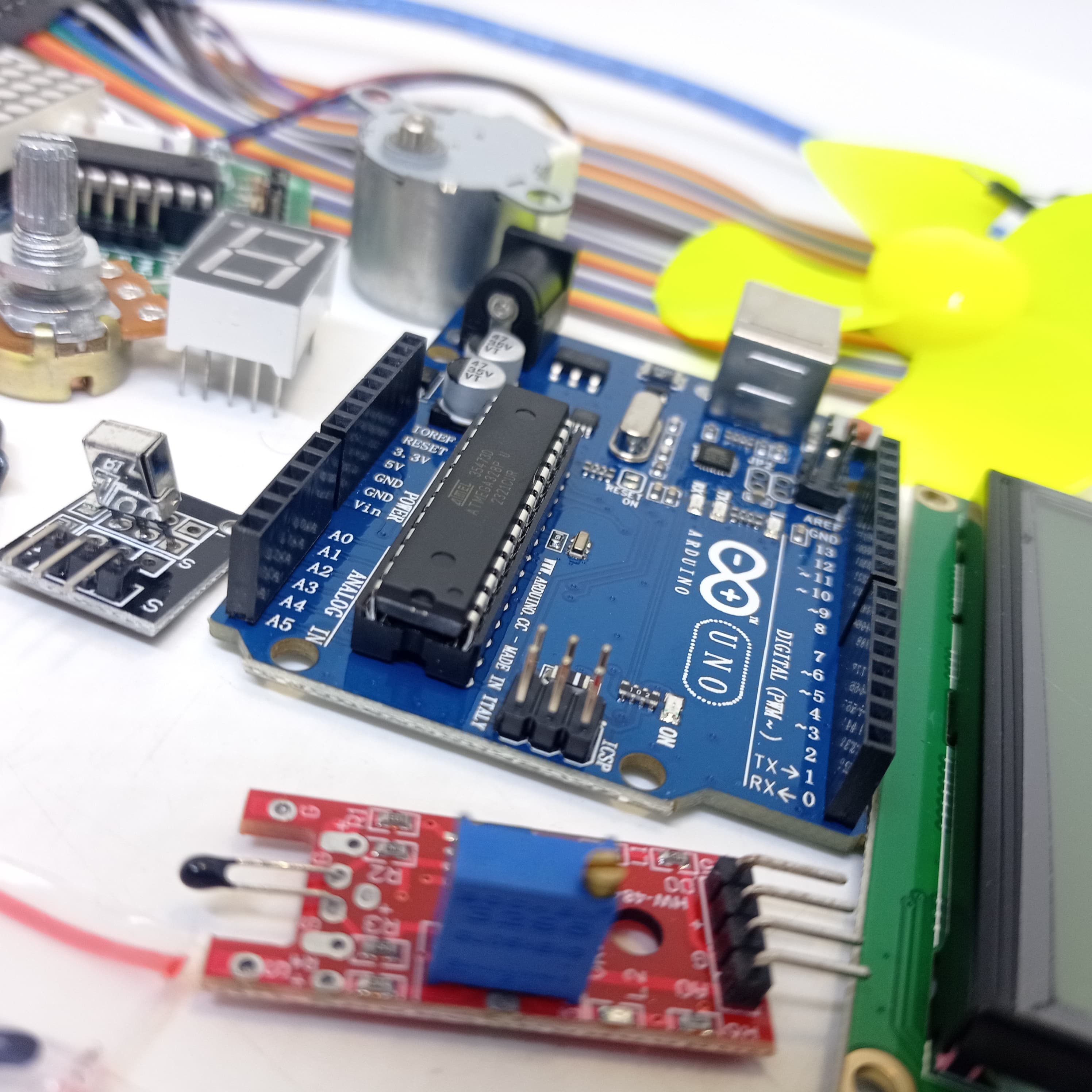 Arduino Starter Kit - a blue Arduino Uno board surrounded by a motor, fan, potentiometer, seven-segment display, sensor module, and LCD screen.