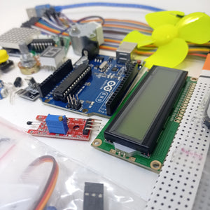Arduino Starter Kit - an Arduino Uno board, an LCD screen, a yellow fan, a sensor module, and various electronic components laid out on a surface.