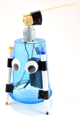 Art Bot - a blue plastic cup robot with googly eyes, three marker legs, a battery pack, and a motor-driven cork with a wooden stick on top.
