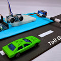 Automatic Car Parking Toll Gate System - an Arduino board, ultrasonic sensor, and servo-controlled barrier arm with two toy cars on a road model.