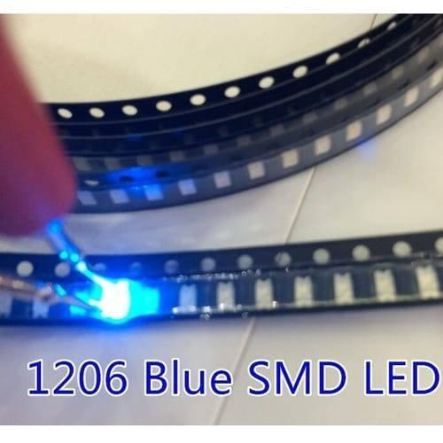 Blue SMD 1206 LED Super Bright Light Emitting Diode - shown as a bright blue light being tested with probes while seated in a black carrier tape reel.
