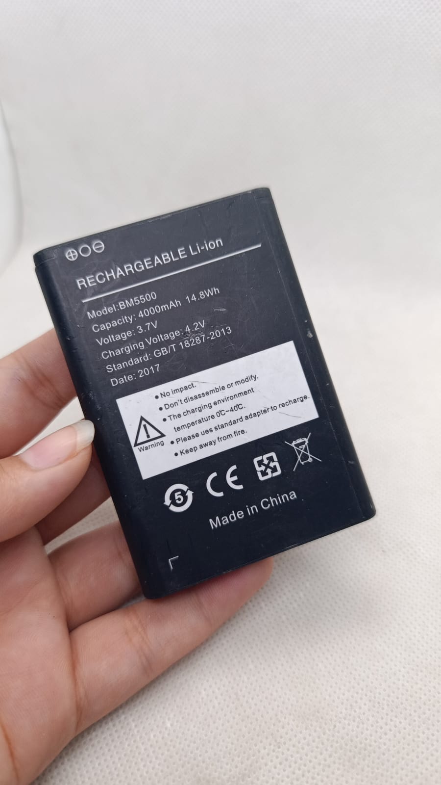 BM5500 3.7V 4000mA Battery - a rectangular black lithium-ion cell held in a hand, showing printed technical specifications and safety warnings on its label.
