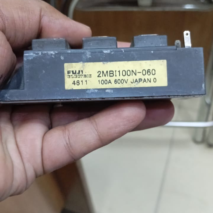 Buy 2MBI100N-060 600V 100A IGBT Module For Local Inverter - held in a hand, featuring a black rectangular casing with a yellow label displaying the model number, 100A, and 600V ratings.