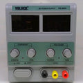 Buy Ps 303A Volder 30V 3A Variable DC Power Supply – Digilog.pk - a grey rectangular device with two blank digital displays, four adjustment knobs, a power button, and three output ports.