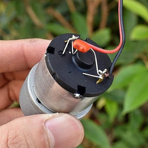 DC 12V 420 RPM With Metal Gears Small Motor - a close-up of the black circular rear end with two soldered power wires and a small orange capacitor.