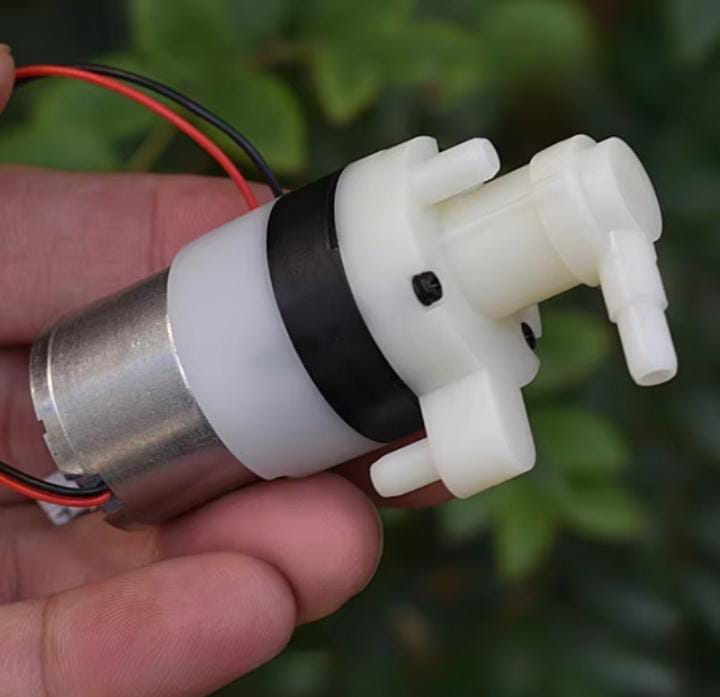 DC 3V-3.7V Pump - shown as a small white plastic pump head attached to a silver cylindrical motor with red and black power wires held in a hand.