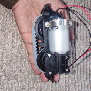 DC Gear Motor With 3.7V To 12V Operated - held in a hand, showing a silver cylindrical motor attached to a black plastic gear assembly with a grey belt.
