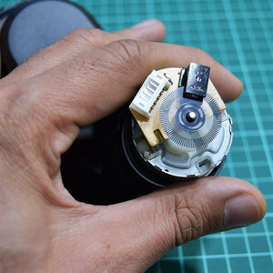DC Gear Motor With Encoder With Wheel - close-up view of the motor rear showing the circular encoder disc, sensor module, and a white connector port.