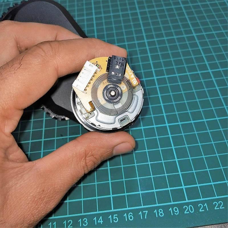 DC Gear Motor With Encoder With Wheel - close-up of the circular encoder disc, circuit board, white connector, and black optical sensor held by a hand.