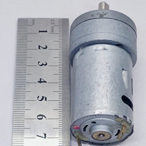 DC Motor DC Electric Geared Motor - shown next to a metal ruler for scale, featuring a cylindrical silver motor body with an attached gear head.