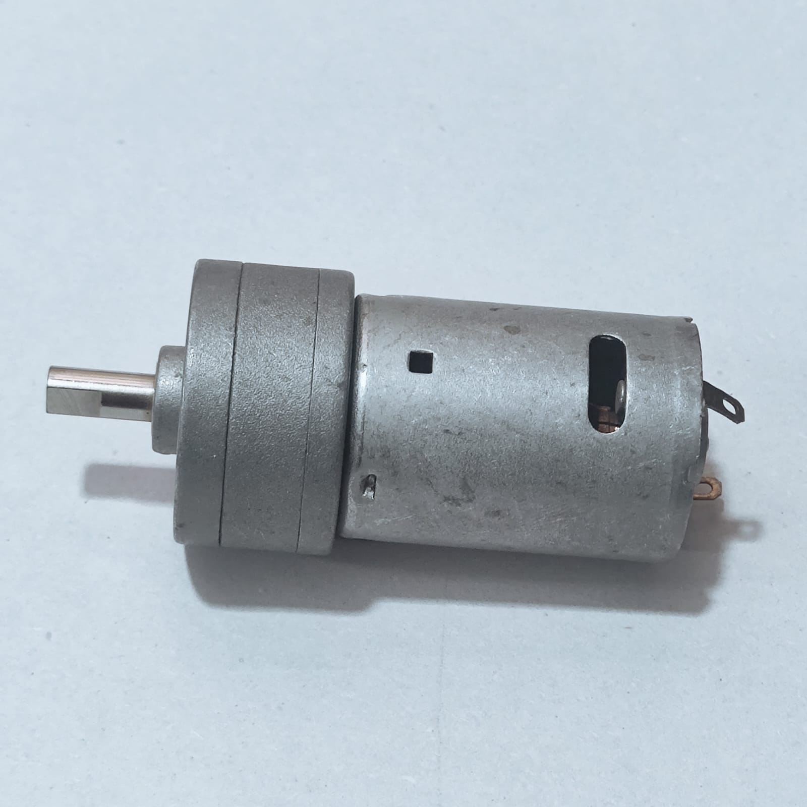 DC Motor DC Electric Geared Motor - shown from the side, featuring a silver cylindrical motor body attached to a metallic gearbox with a D-shaped output shaft.