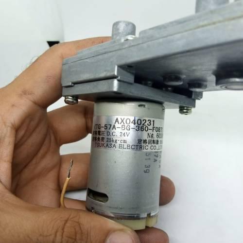 DC Worm Gear Motor AXO40231 - held in a hand, showing the silver cylindrical motor body with a printed label and an attached metal gearbox assembly.