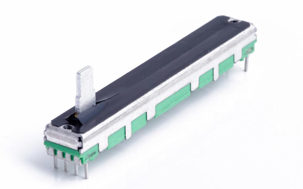 Digilog.pk - Slide Potentiometers B10K | Single Potentiometers & Variable Resistors Pakistan - a long, rectangular variable resistor with a metal slider, green base, and silver pins on a white background.