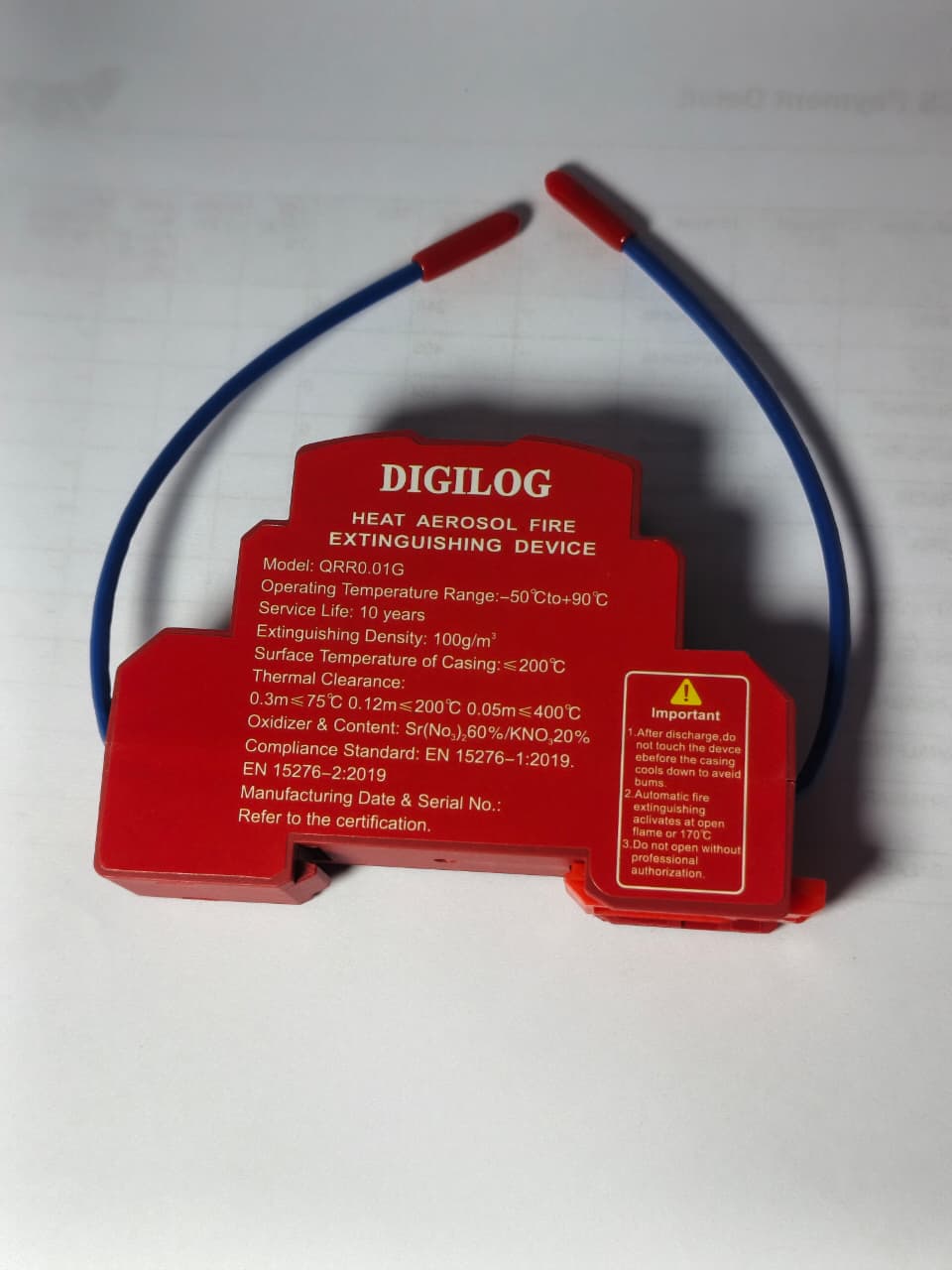 DIGILOG QRR0.01G Heat Aerosol Fire Extinguishing Device - a red, rectangular unit with a blue wire loop and printed technical specifications on its face.