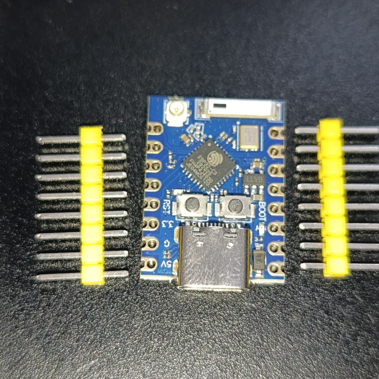 Discontinued ESP32 C3 Pro Mini WiFi Bluetooth Development Board 4MB - Risc-v IOT Microcontroller - with a blue PCB, USB-C port, two buttons, and two separate rows of yellow-cased header pins on a dark surface.