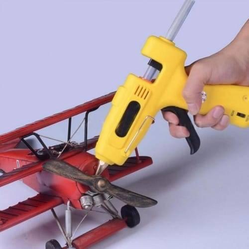 DIY Hot Melt 7mm Glue Stick - a yellow glue gun with a trigger and power switch, is shown being used to glue a propeller onto a red model airplane.