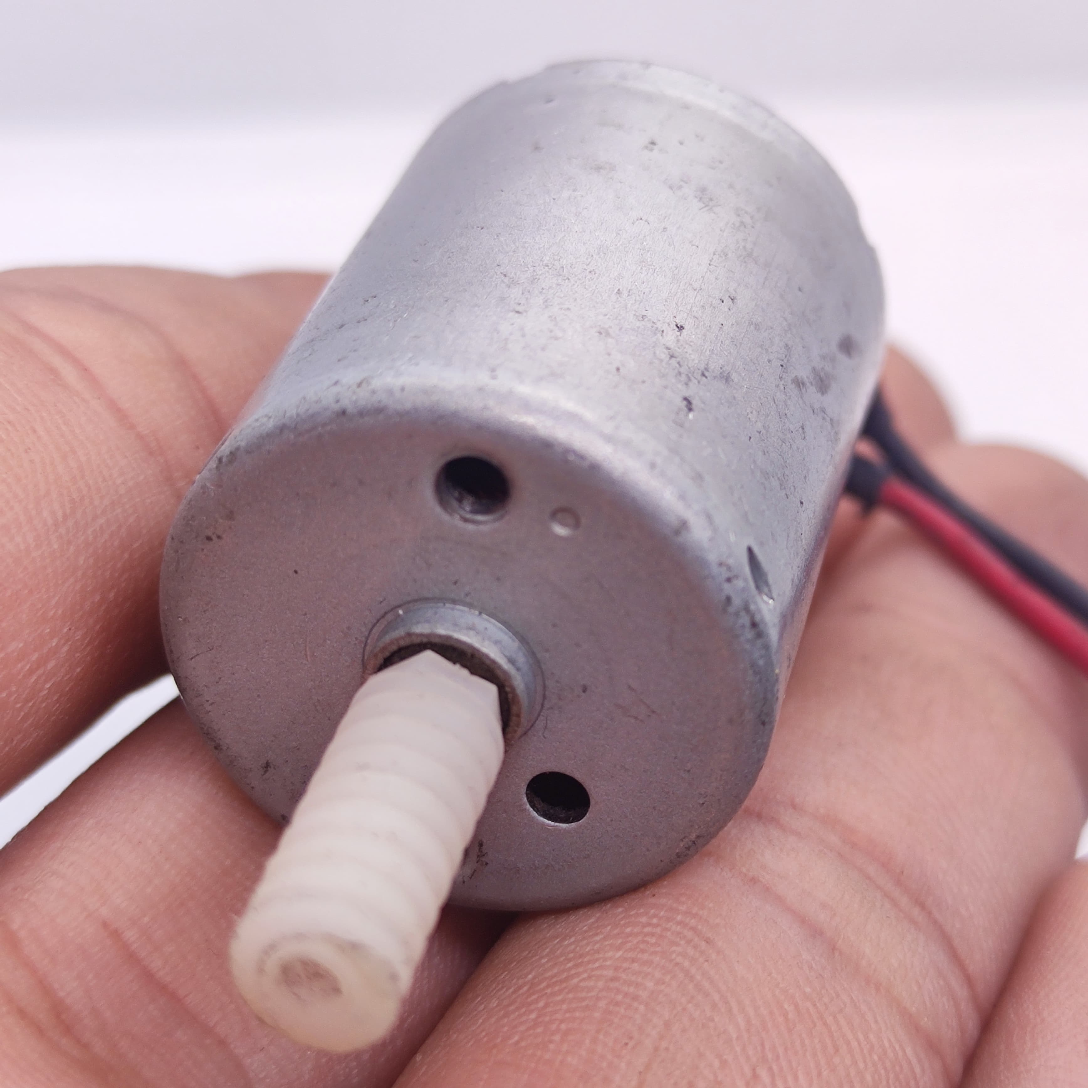 DIY Mini 5vdc DC Motor - a close-up showing a silver cylindrical motor body with a white plastic worm gear on the shaft and red and black power wires.