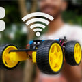 DIY Simple WiFi Controlled Robot Car Parts Not Pre Assembled - shown as a partially assembled yellow-wheeled robot chassis held against a blurred background.